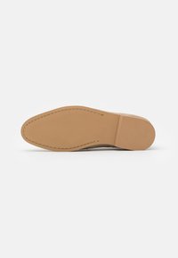 Suede sko i en lys beige farge med en glatt lærsåle. Merkelig søm langs kanten og en rund tådesign.