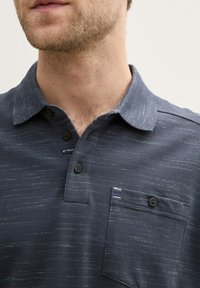 Granatowa koszula polo o teksturowanej tkaninie, z kołnierzykiem, trzema guzikami i kieszenią na piersi z paskowanym wykończeniem.