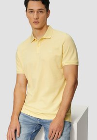 Polo shirt jaune en coton, avec une finition texturée, un col côtelé et un petit logo brodé sur la poitrine gauche.
