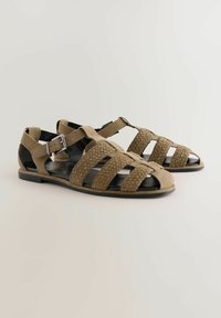 Sandale din piele împletită de culoare bej, cu design cu vârf deschis, multiple curele, cataramă ajustabilă la glezne și talpă din cauciuc negru.