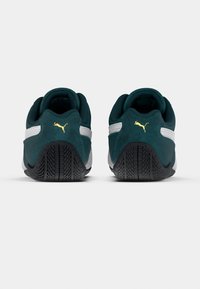 Baskets en daim vert avec des accents blancs, dotées d'une semelle en caoutchouc noire et d'un logo doré. Texture lisse avec un design à profil bas.