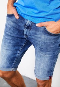 Shorts de mezclilla en azul claro con un acabado desgastado, con puños enrollados y bolsillos frontales. Textura suave con detalles de costura.