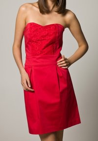 Robe rouge sans bretelles avec un corsage en dentelle florale, jupe plissée et tissu lisse ; sa conception ajustée et sa coupe à mi-cuisse mettent en valeur la silhouette.
