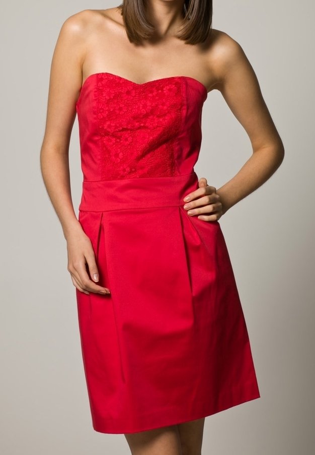 Robe rouge sans bretelles avec un corsage en dentelle florale, jupe plissée et tissu lisse ; sa conception ajustée et sa coupe à mi-cuisse mettent en valeur la silhouette.