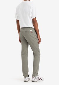 Szare bawełniane spodnie o prostych nogawkach, z tylnymi kieszeniami i widocznym logo. Połączone z białym T-shirtem i sportowymi butami.