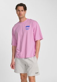 Rosa kortärmad t-shirt i bomull. Har en blå grafisk tryck på bröstet. Matchad med ljusgrå shorts. Enkel, avslappnad passform.