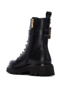 Botín negro de cuero con suela gruesa, que cuenta con un zipper lateral y un acento decorativo de hardware dorado. Los cordones se extienden hasta la mitad de la altura.