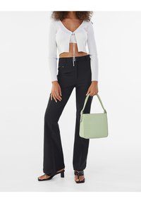 Vitt ribbat crop top med snörning, svarta utsvängda byxor och en ljusgrön väsk av imitationsläder med ett strukturerat krokodilmönster.