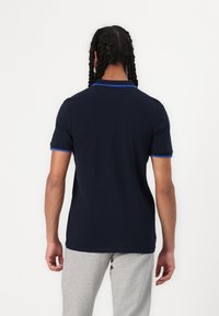 Polo bleu marine avec un col et des accents de manches bleu clair contrastants. Matière en coton lisse, coupe standard, manches courtes.