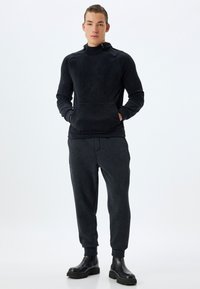 Svart fleece hoodie med hög krage och framficka, tillsammans med svarta fleece-joggers. Slät textur, figurnära design, elastiska ärmslut.