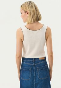 White sleeveless top with textured fabric and black trim at the neckline, paired with a blue denim skirt featuring back pockets.