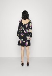 Vestido preto floral com mangas longas, apresentando flores multicoloridas, costas em quadrado e uma bainha em camadas. Combinado com sapatos de salto alto pretos.