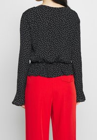 Top a maniche lunghe nero a pois con orlo a volant abbinato a pantaloni rossi a vita alta. Presenta un colletto rotondo e una vestibilità comoda.