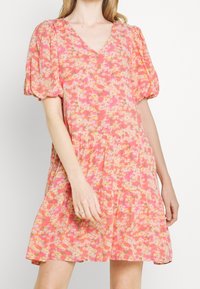 Blumenkleid in Pink- und Orangetönen mit Puffärmeln, V-Ausschnitt, gestuftem Rock und leichtem Stoff, der kleine Gänseblümchenmuster aufweist.