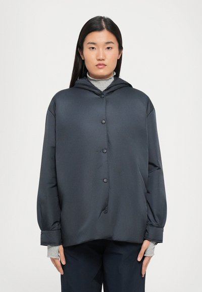 Giacca a hood grigio scuro con bottoni frontali, vestibilità rilassata e polsini elasticizzati. Tessuto liscio, design minimalista, abbinata a una maglia grigia chiara.
