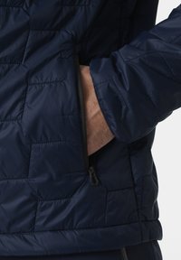 Námořnická modrá prošívaná bunda s texturou, boční kapsou se zipem a elastickými manžetami pro pohodlné nošení.