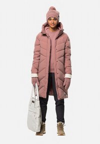 Rosa Pufferjacke mit Zickzackmuster, gestrickte rosa Mütze, graue Handtasche, braune Stiefel und passende Handschuhe. Die Schichten beinhalten einen rosa Sweatshirt.