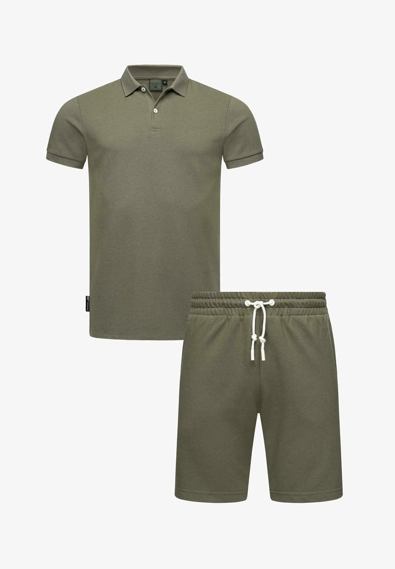 Olīvzaļa polo krekls ar īsām piedurknēm un apkakli, apvienots ar saskaņojošām aizvelkamo īsās biksēm. Abi ir izgatavoti no mīkstas, teksturētas auduma.