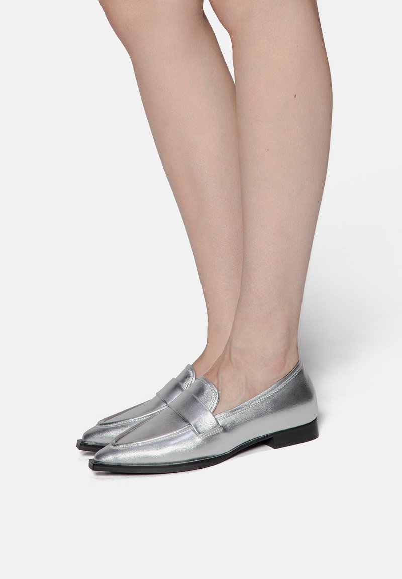 Silver metallic loafers with a sleek design, pointed toes, and a decorative strap across the front; smooth texture, low flat heel.