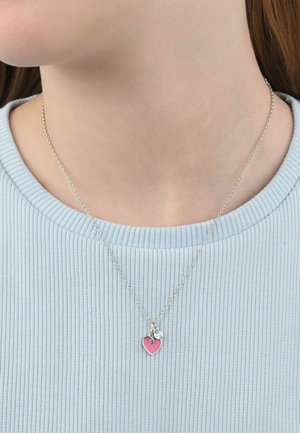Collar de cadena plateada con un pequeño corazón rosa y un diminuto colgante redondo, llevado sobre una camiseta azul claro acanalada.