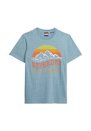 Lichtblauw katoenen T-shirt met een grafisch ontwerp van bergen en een zon in oranje en geel, met de tekst "SUPERDRY MFG CO QUALITY GARMENTS" in vetgedrukt.