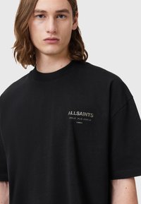 Zwarte katoenen T-shirt met een ronde hals, korte mouwen en geborduurd "ALLSAINTS" logo in een metallic lettertype op de borst.