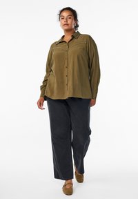 Olive green button-up shirt with a relaxed fit, featuring decorative stitching on the collar, paired with dark wide-leg pants and brown shoes.
