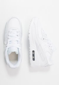 Zapatillas blancas con parte superior sintética lisa, detalles en azul claro, cierre de cordones, cuello acolchado y una unidad de aire visible en la suela.