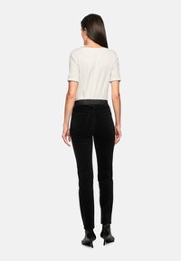 Schwarze Samthose mit weicher Textur, hohem Bund und schmaler Passform, kombiniert mit einem hellen cremefarbenen Kurzarmtop.