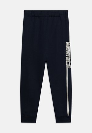 Marineblå joggebukser med elastisk midje og mansjetter; har en kontrasterende vertikal stripe med "VERSACE" trykket i hvitt på venstre side.