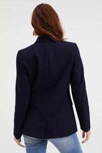 Námornícky blazer se strukturovanými klopami a přiléhavým střihem. Má jeden rozvent na zadní straně a jemné dekorativní detaily na manžetách.