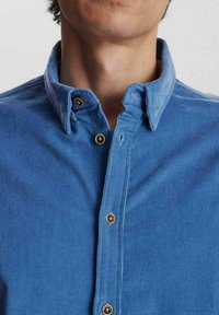 Camisa de botones azul con un tejido suave y texturizado. Presenta un cuello clásico, dos botones en el cuello y un diseño ajustado.