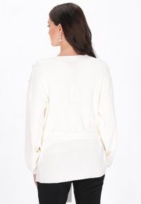 Biały sweter z dzianiny z długimi rękawami, dekoltem w serek, w prążkowanej fakturze, z perłowymi akcentami na ramionach i wiązaniem w talii.