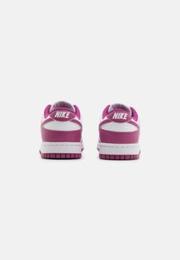 Nike sportcipő, fehér felső résszel, rózsaszín díszítésekkel és strukturált gumitalppal. Kiemelkedő jellemzői közé tartozik a párnázott bokarész és a feltűnő logó.