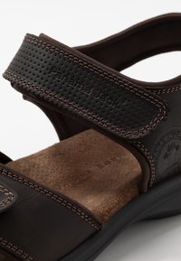 Sandalo in pelle marrone con due cinturini regolabili, una soletta testurizzata e cuciture a contrasto, caratterizzato da un logo impresso sul lato.