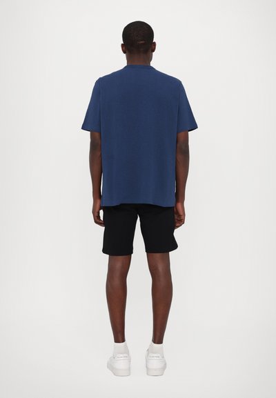Chemise bleu marine à manches courtes en tissu doux, associée à un short noir. La tenue présente une coupe décontractée et arrive à la hanche.