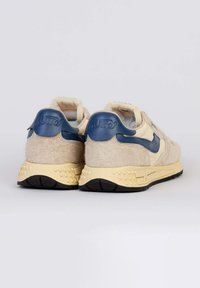 Sneakers in camoscio beige con accenti in pelle blu navy e suola gialla testurizzata. Caratteristiche includono un colletto imbottito e il logo del marchio inciso sul tallone.