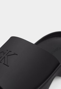 Μαύρο σανδάλι τύπου slide με ανάγλυφο λογότυπο CK στον φαρδύ ιμάντα και υφή στην ποδόστρωμα.