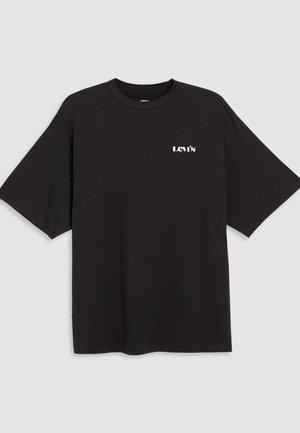 Μαύρο κοντομάνικο t-shirt Levi's με λευκό λογότυπο τυπωμένο στο αριστερό στήθος, εμφανίζεται σε ανοιχτό γκρι φόντο.