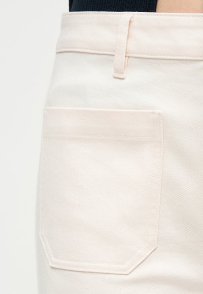 Κοντινό πλάνο τσέπης από ανοιχτό μπεζ τζιν παντελόνι με θηλιά ζώνης και επάνω ραφή σε ένα άτομο που φοράει σκούρο τοπ.