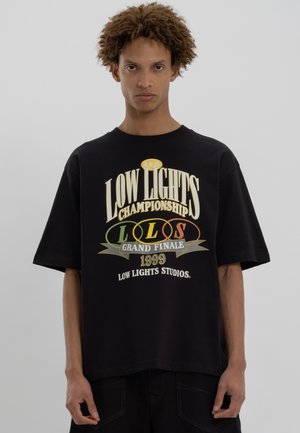 Černé oversized tričko vyrobené z bavlny s odvážným grafickým potiskem v žluté, zelené a červené barvě, obsahující text a logo spojené s "Low Lights Studios."