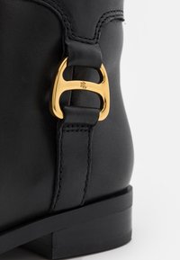 Talons de bottes en cuir noir avec une boucle métallique dorée gravée "RL" sur la sangle latérale.