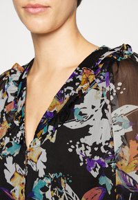 Blusa preta floral com decote franzido, com padrões abstratos coloridos em roxo, verde-água, laranja e branco sobre um tecido transparente.