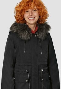 Schwarze isolierte Jacke mit einer Kapuze aus Kunstfell. Verfügt über einen Kordelzug in der Taille, mehrere Taschen und silberne Akzente für ein praktisches Design.