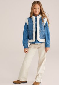 Gilet in denim con fodera in sherpa bianca, design senza maniche, due tasche frontali, abbinato a una camicia in denim blu e pantaloni a palazzo color crema.
