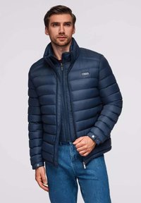 Marinefarbener Puffer-Jacke mit horizontalen Nähten, hohem Kragen und frontalem Reißverschluss. Verfügt über Seitentaschen und Druckknopfmanschetten. Leichtes Material.