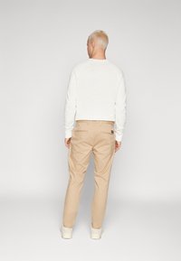 Sweatshirt blanc court à manches longues, associé à un pantalon beige clair. La tenue est complétée par des baskets blanches avec des accents.