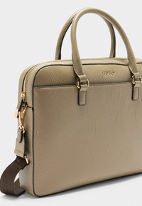 Olijfgroene leren tas met twee handvaten bovenaan, hardware in goudkleur, ritssluiting en een afneembare schouderriem. Textuurdetail op het oppervlak.