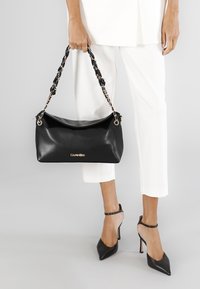 Sort læderhåndtaske med en glat overflade, der har en flettekæderem og diskrete detaljer i guldhardware.