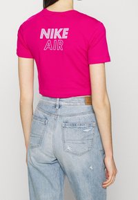 Kvinna som bär en ljusrosa, kortärmad Nike-tröja och ljusblå, hög midja jeans, står med ryggen vänd mot kameran.